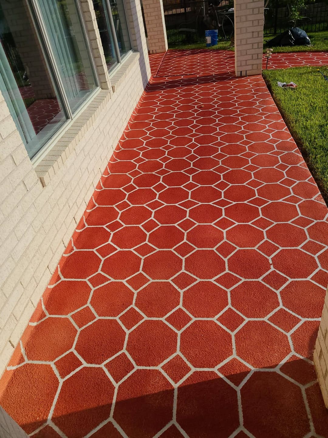 Vibrant red and white hexagonal patterned concrete walkway beside brick wall and green grass.