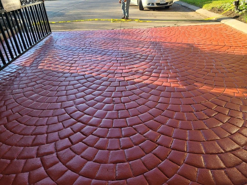 Red stamped concrete driveway with a circular pattern, gate visible in the background.
