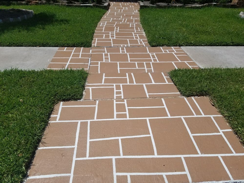 Decorative brown stone walkway with white grout lines surrounded by green grass.